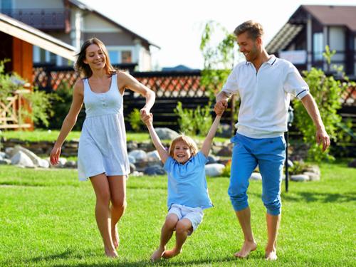 Mutter, Vater, Kind auf einer Wiese vor dem Ferienhaus